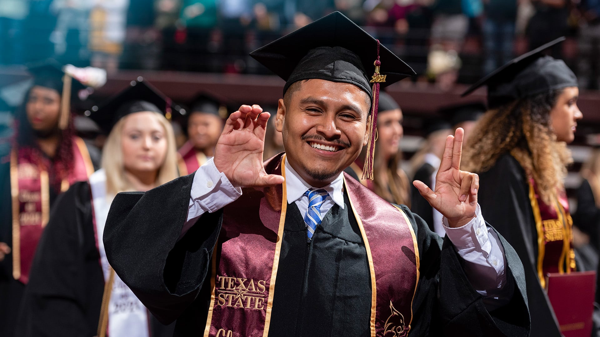 Student smiling at commencement holding Texas State hand sign
